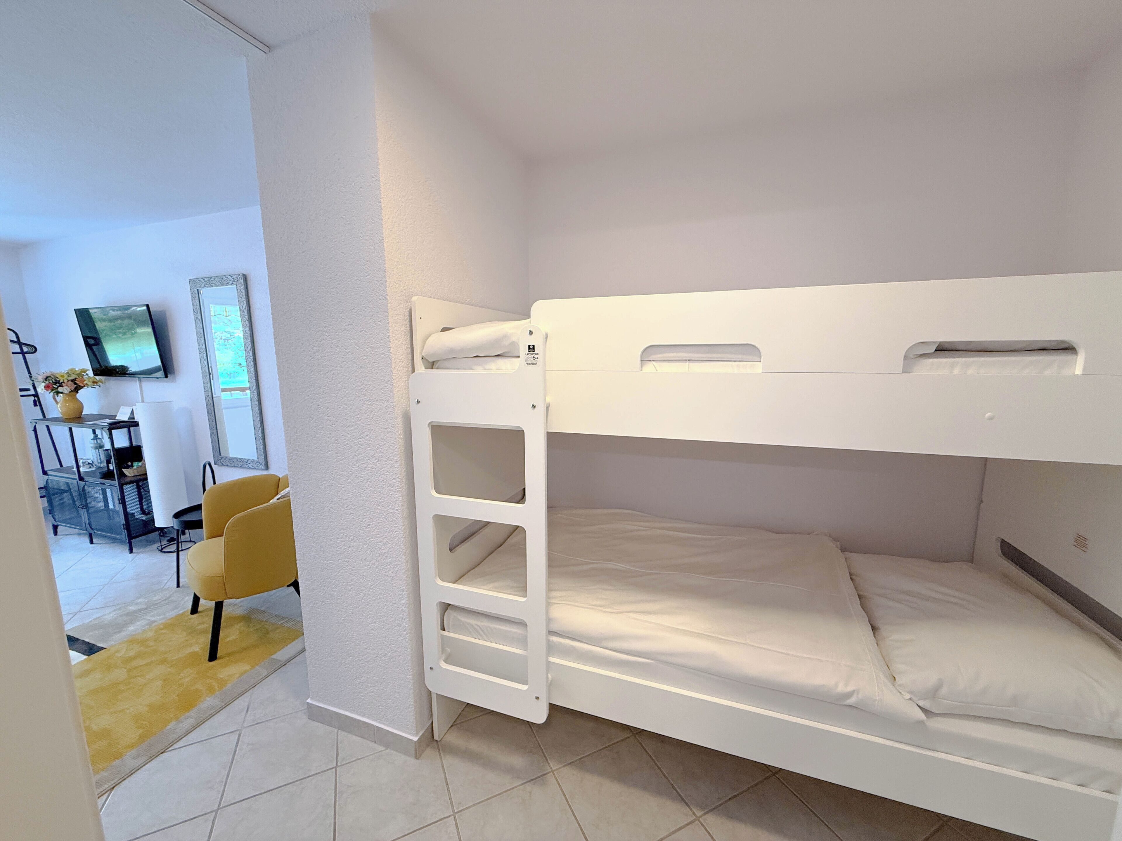 A bunk bed room with a desk and chair, a television, and a window.