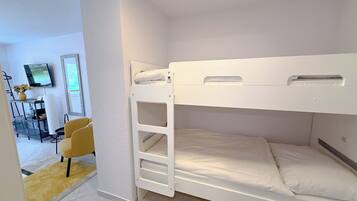 A bunk bed room with a desk and chair, a television, and a window.