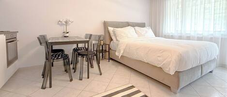 A bedroom with a bed, a desk, chairs, and a small table with a plant.