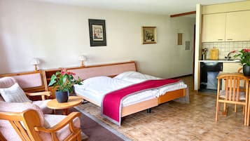 A bedroom with a bed, a sofa, a dining table, and a kitchen area.
