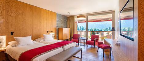 Una habitación de hotel con una cama grande, un banco, un escritorio y un balcón con sillas rojas.