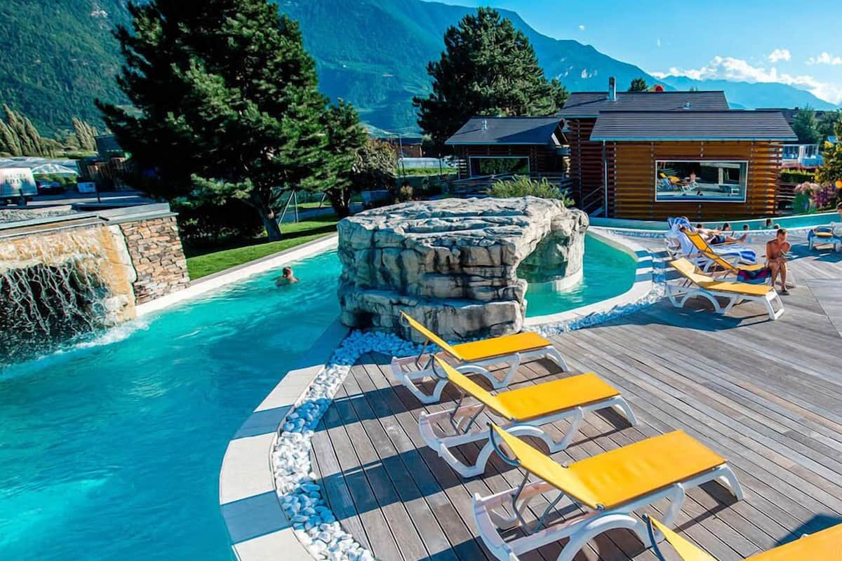 A pool area with wooden deck and lounge chairs, surrounded by mountains.
