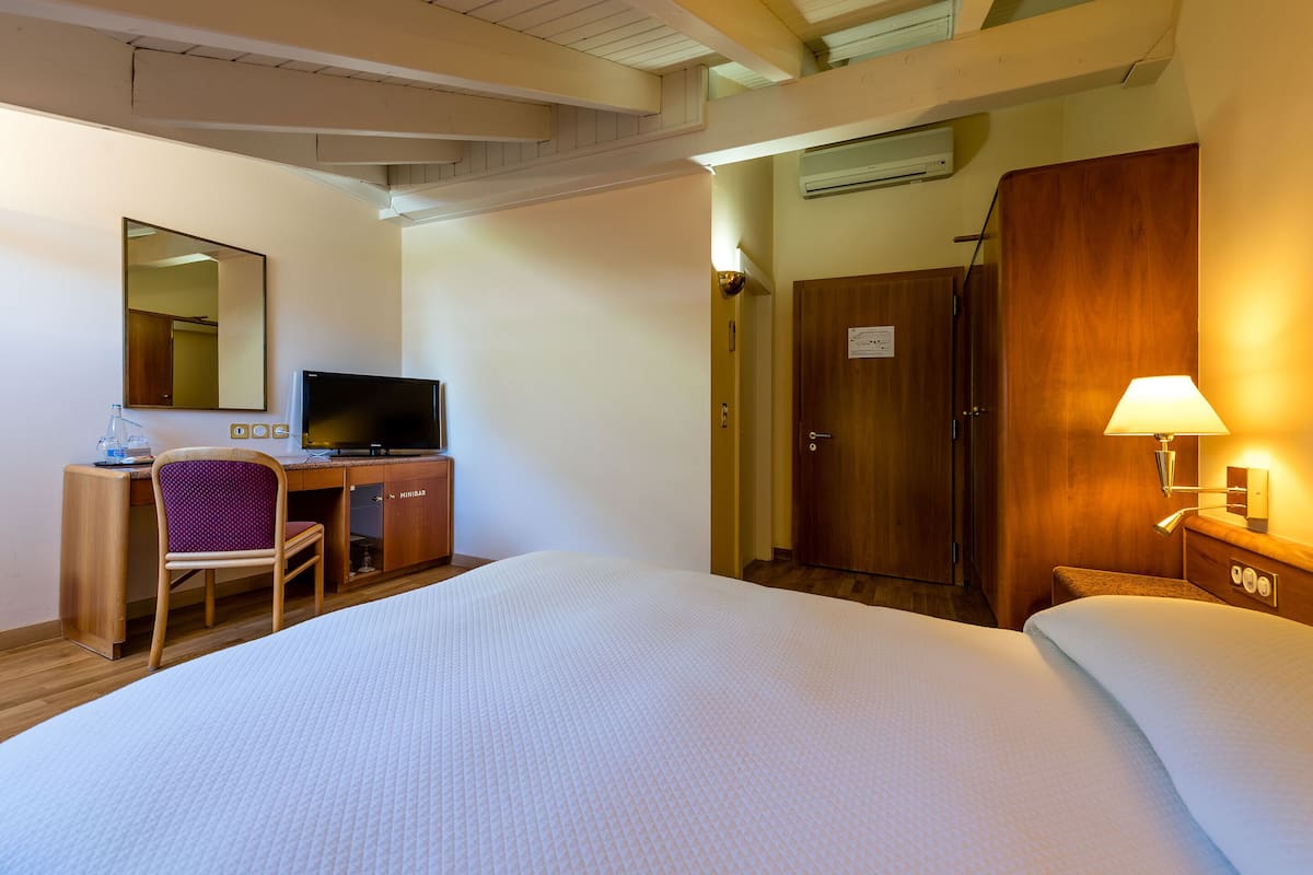 A hotel room with a bed, a desk with a computer, a chair, a wardrobe, and a mirror.