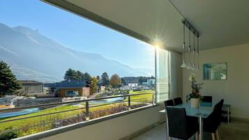 A modern room with a large window offering a mountain view, a dining area with chairs and a table, and a ceiling light fixture.