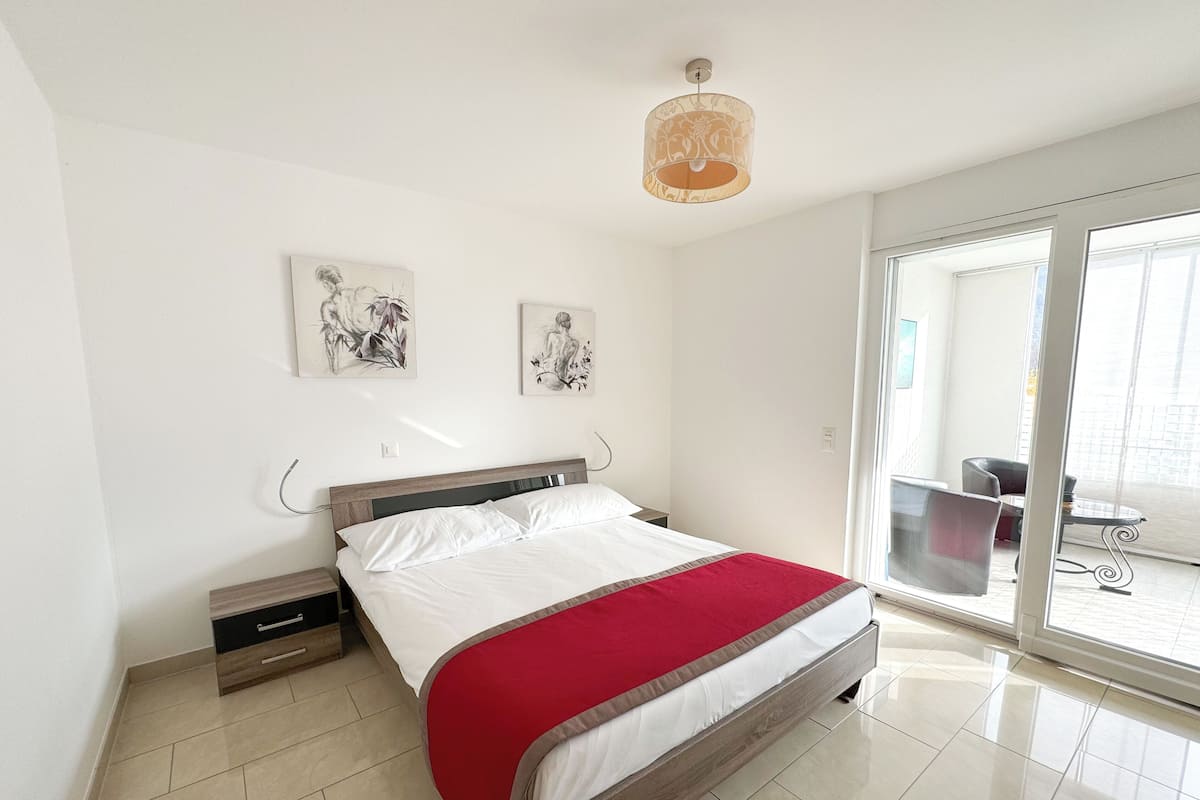 A modern bedroom with a bed, a nightstand, a red throw blanket, and two wall art pieces.