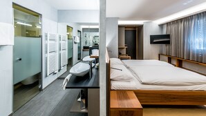 Et moderne hotelværelse med en træseng, et stort spejl, en vask og et fladskærms-TV.