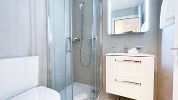 A modern bathroom with a glass-enclosed shower, a white toilet, and a vanity with a mirror above it.