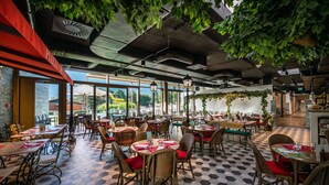 En restaurant med sekskantet gulvbelægning, fletstole med røde hynder og store vinduer med udsigt til det fri.