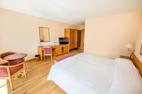 Una habitación de hotel con una cama, un escritorio con ordenador, una silla y una mesita.