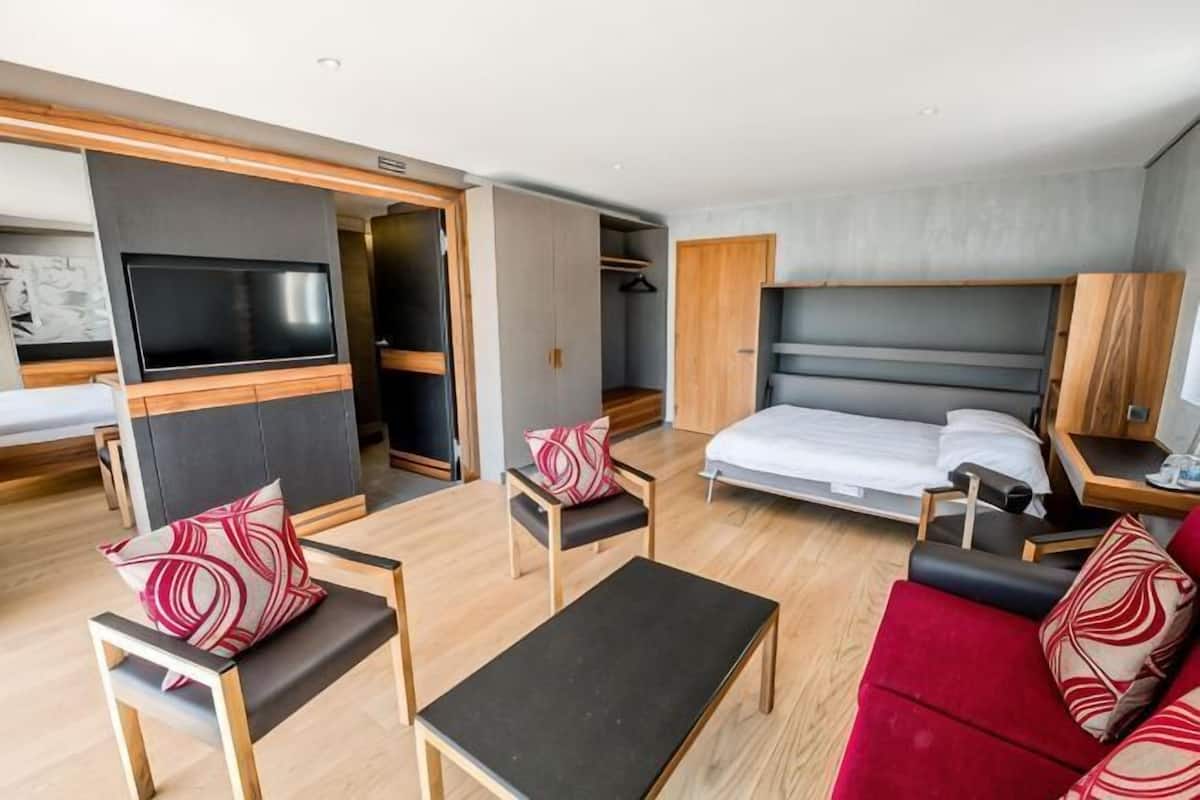 A hotel room with a bed, a TV, a desk, a chair, a sofa, and a wardrobe.