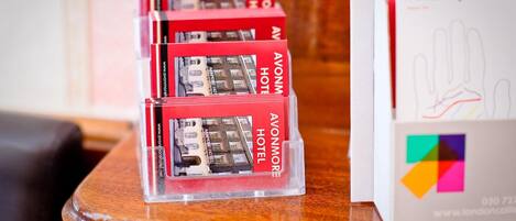 A stack of red brochures for the Avonmore Hotel on a wooden table, with a tube map brochure beside it.