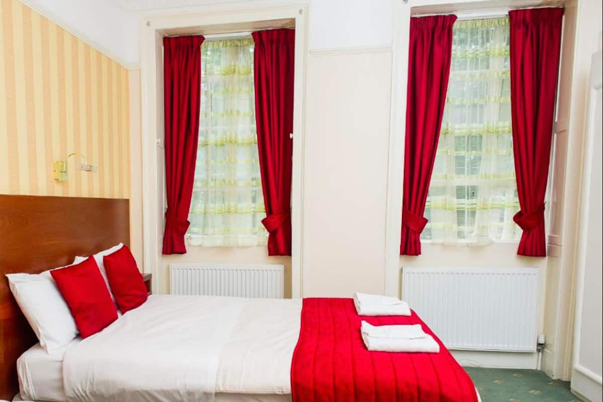A hotel room with a bed, red curtains, a radiator, and a striped wall.