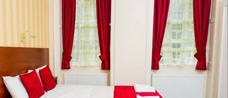 Una habitación de hotel con una cama, cortinas rojas, un radiador y una pared a rayas.