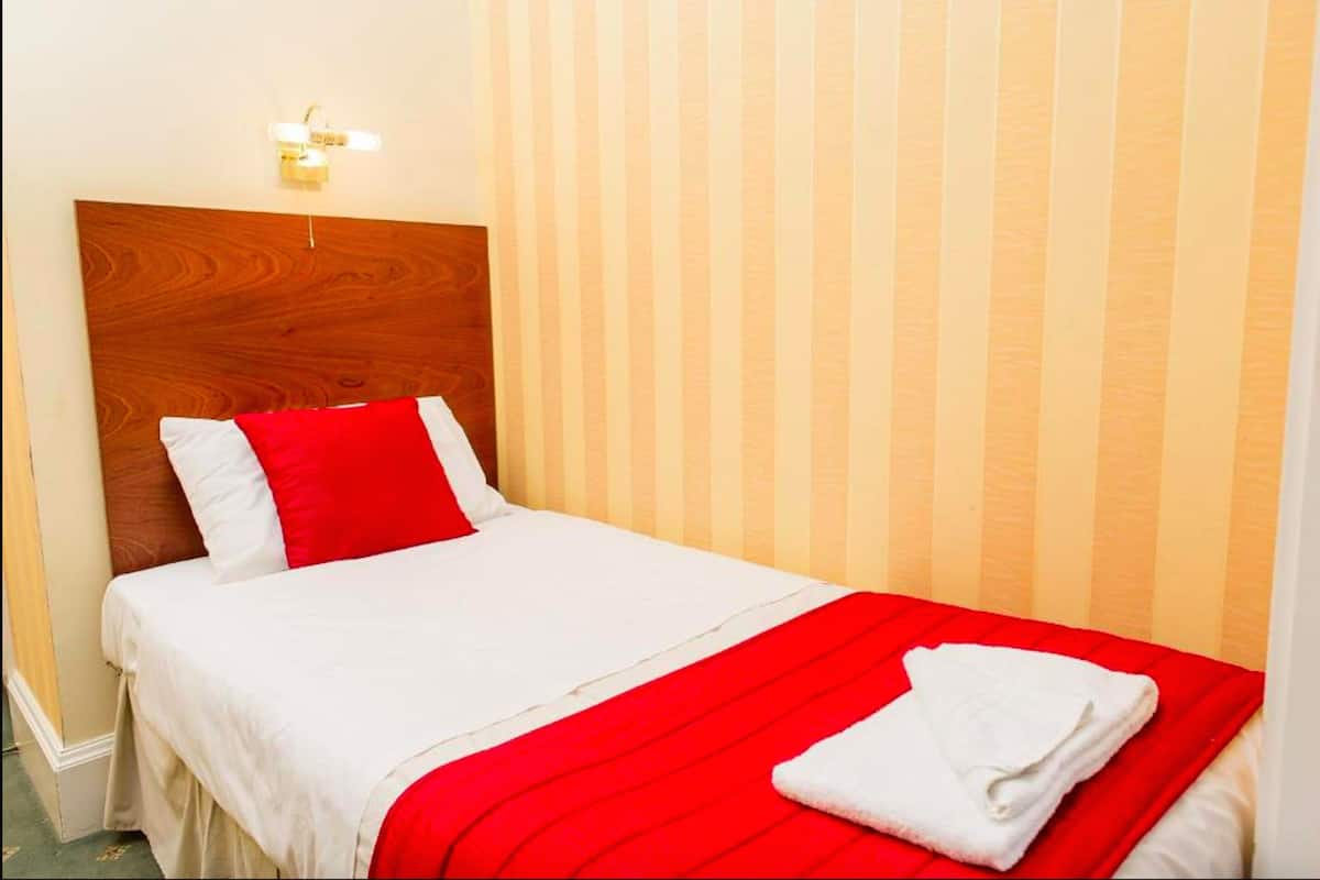 A neatly made bed with white and red bedding, a wooden headboard, and a striped wall in the background.