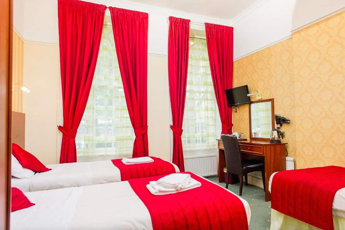A hotel room with two beds, red curtains, a desk with a chair, a television, and a window with a view.