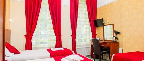 Habitación de hotel con dos camas, cortinas rojas, un escritorio con silla, televisor y ventana con vistas.