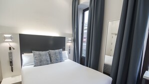 Una habitación de hotel con una cama grande, un teléfono en la mesita de noche y una ventana con cortinas.