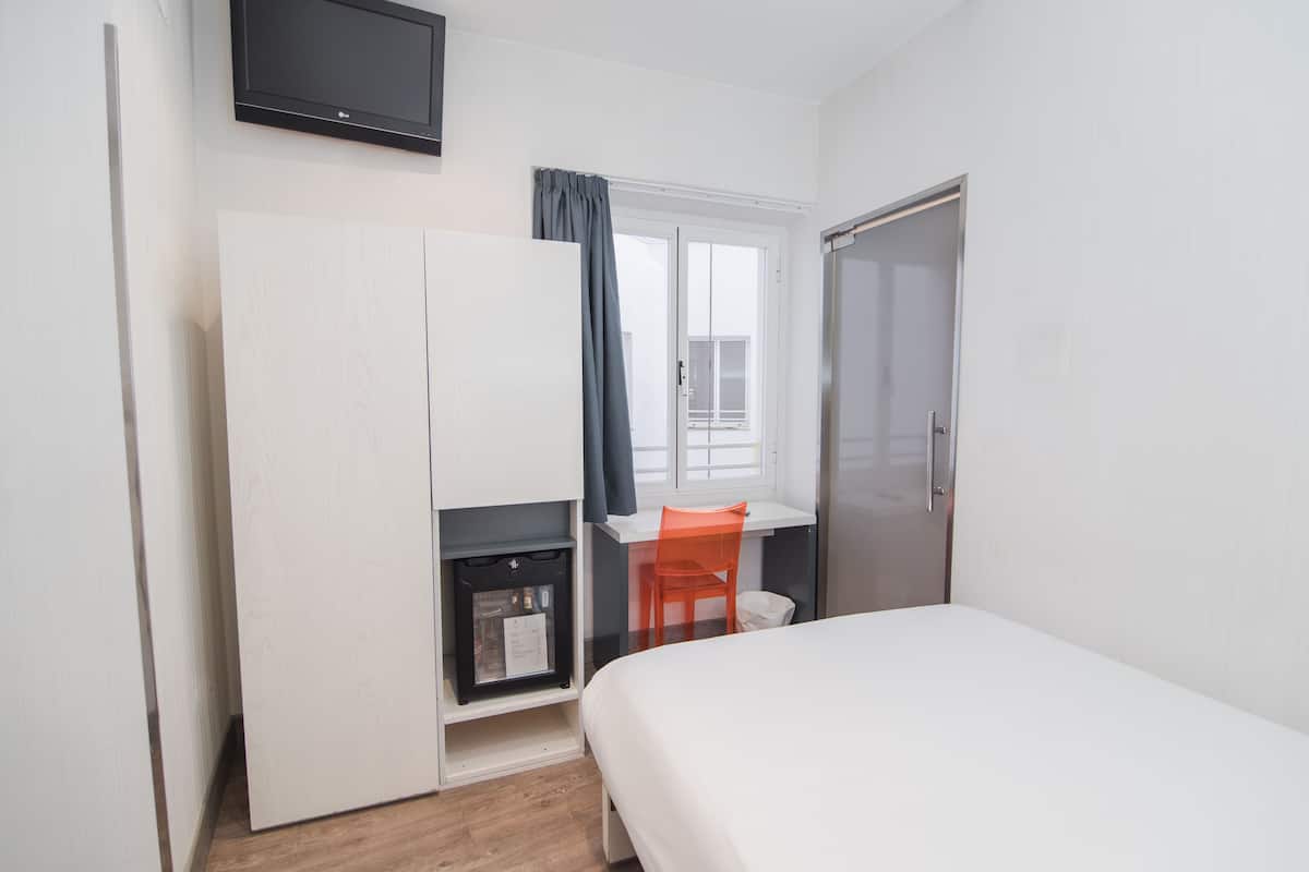 A bedroom with a bed, a desk with a chair, a wardrobe, a television, and a window with curtains.