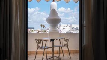 An open balcony with a table and chairs, a white column, and a view of buildings and palm trees.