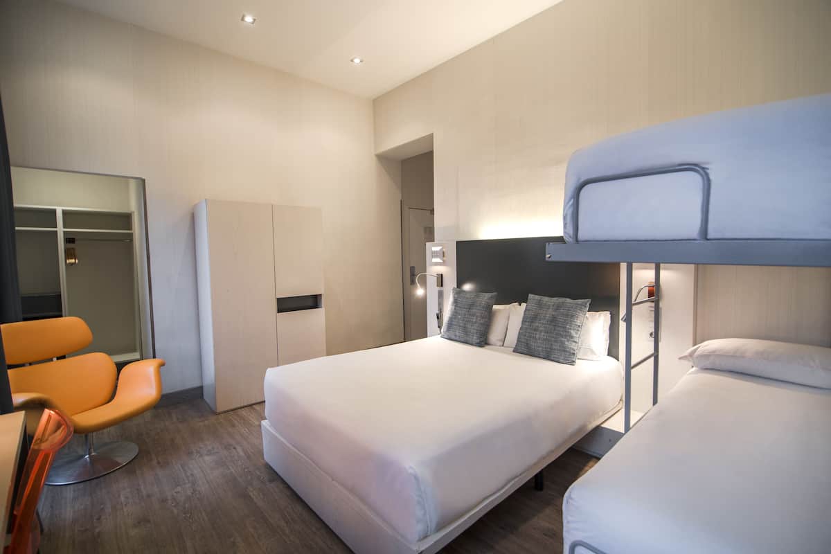 A modern hotel room with a large bed, a bedside table, a chair, and a wardrobe.