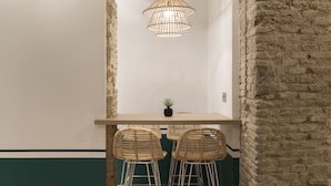 Una habitación con una mesa de madera, dos sillas de mimbre, una lámpara colgante y una pequeña planta en maceta.