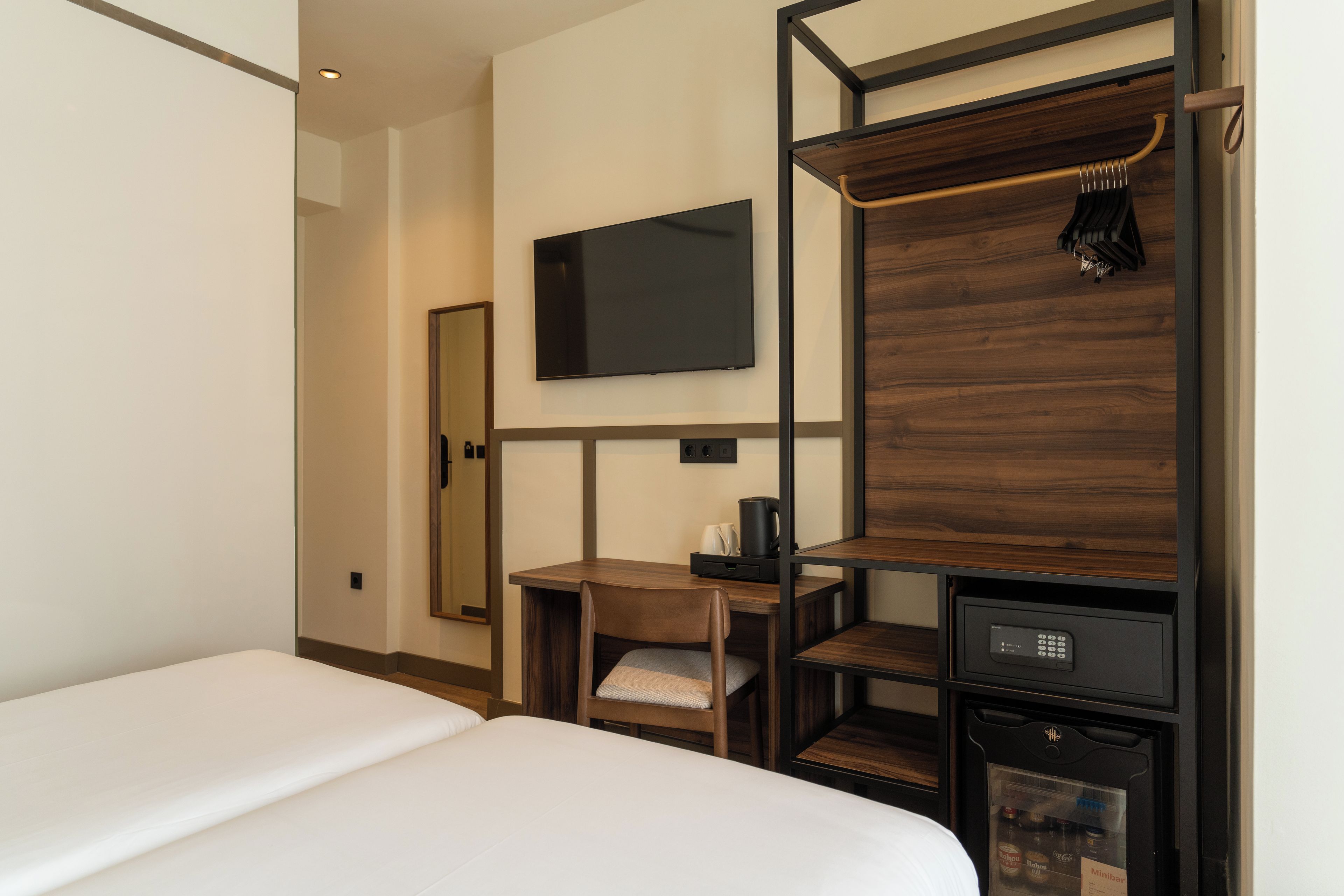 Habitación de hotel con cama, escritorio con silla, televisión, minibar y perchero.