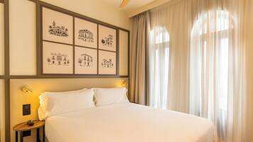 Habitación de hotel con una cama grande, una mesita de noche con lámpara y una pared decorada con dibujos arquitectónicos en blanco y negro.