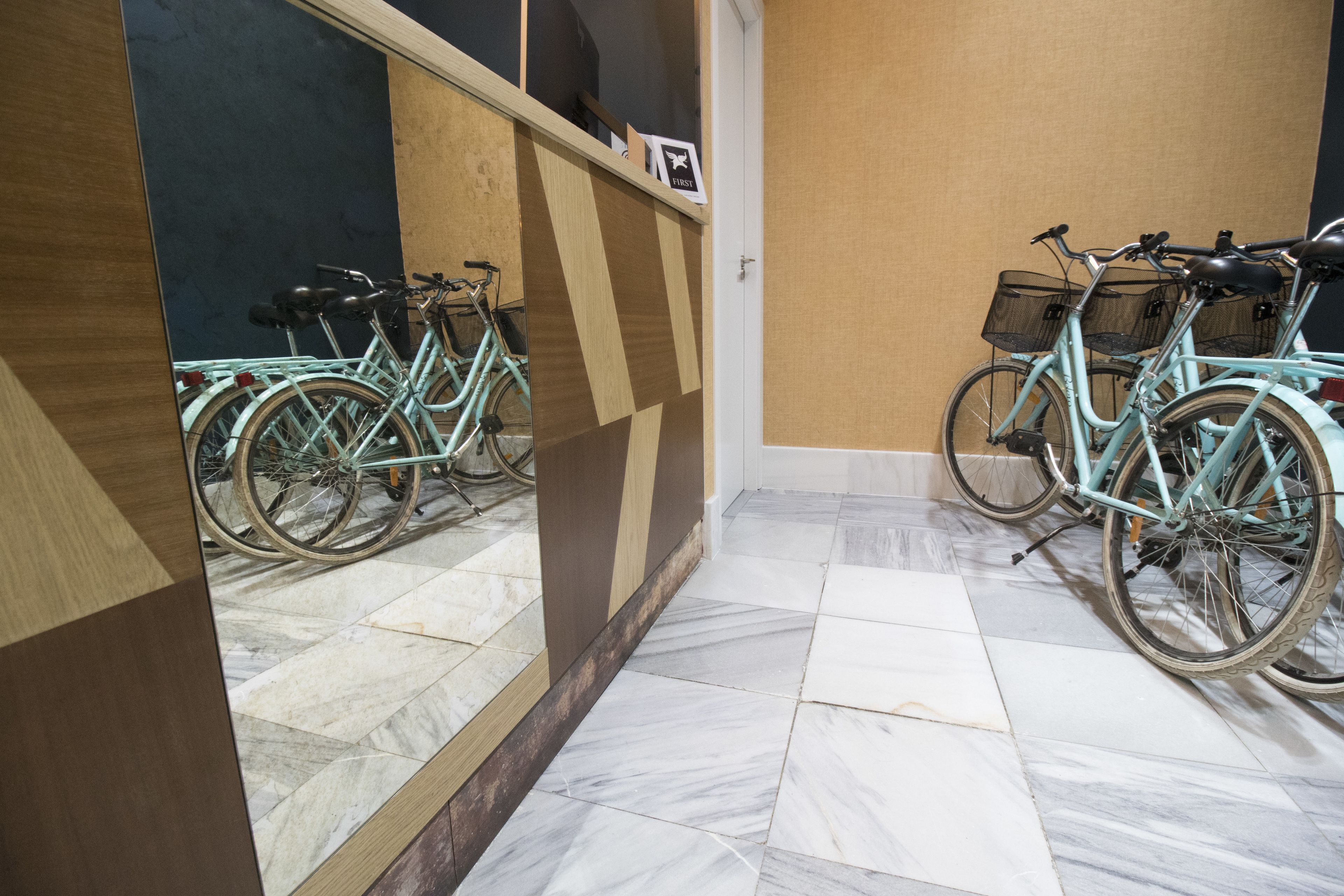 A hallway with a tiled floor and a mirror reflecting bicycles.