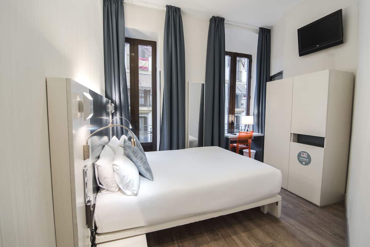 A modern hotel room with a bed, a desk, and a television.