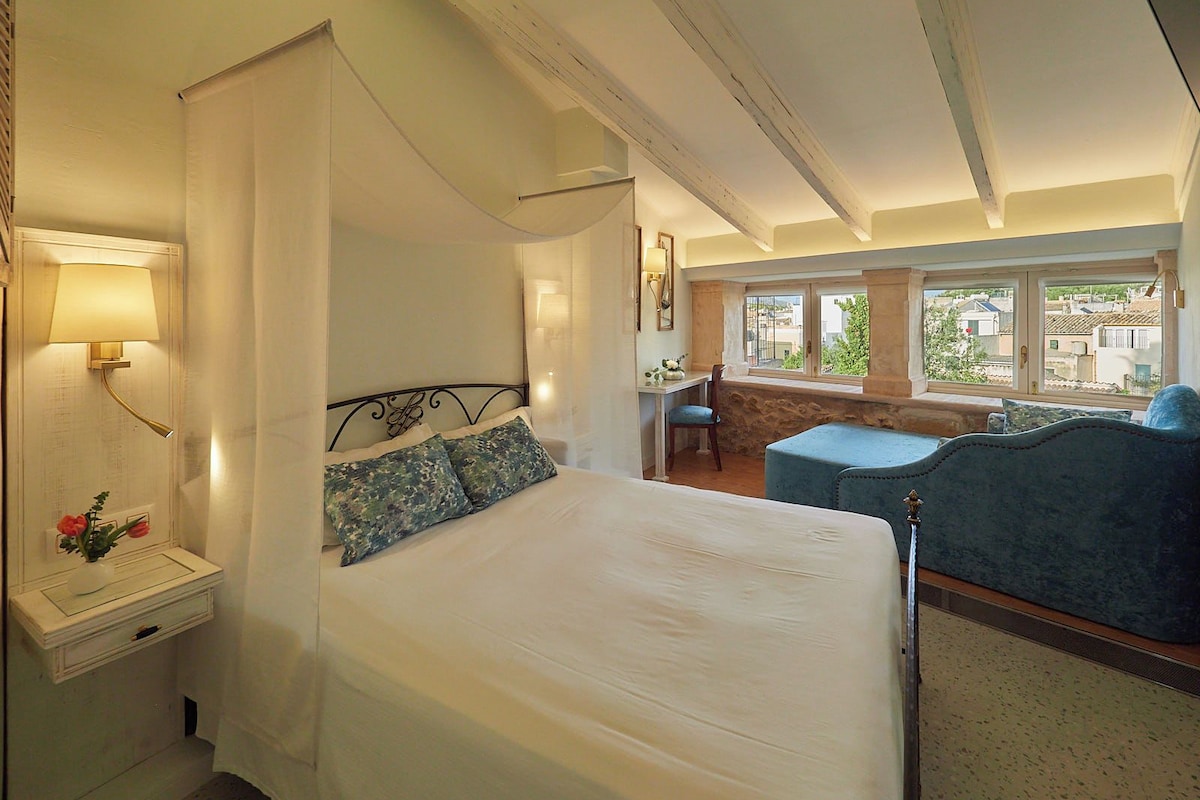 Un dormitorio con cama con dosel, un escritorio y vistas al exterior.