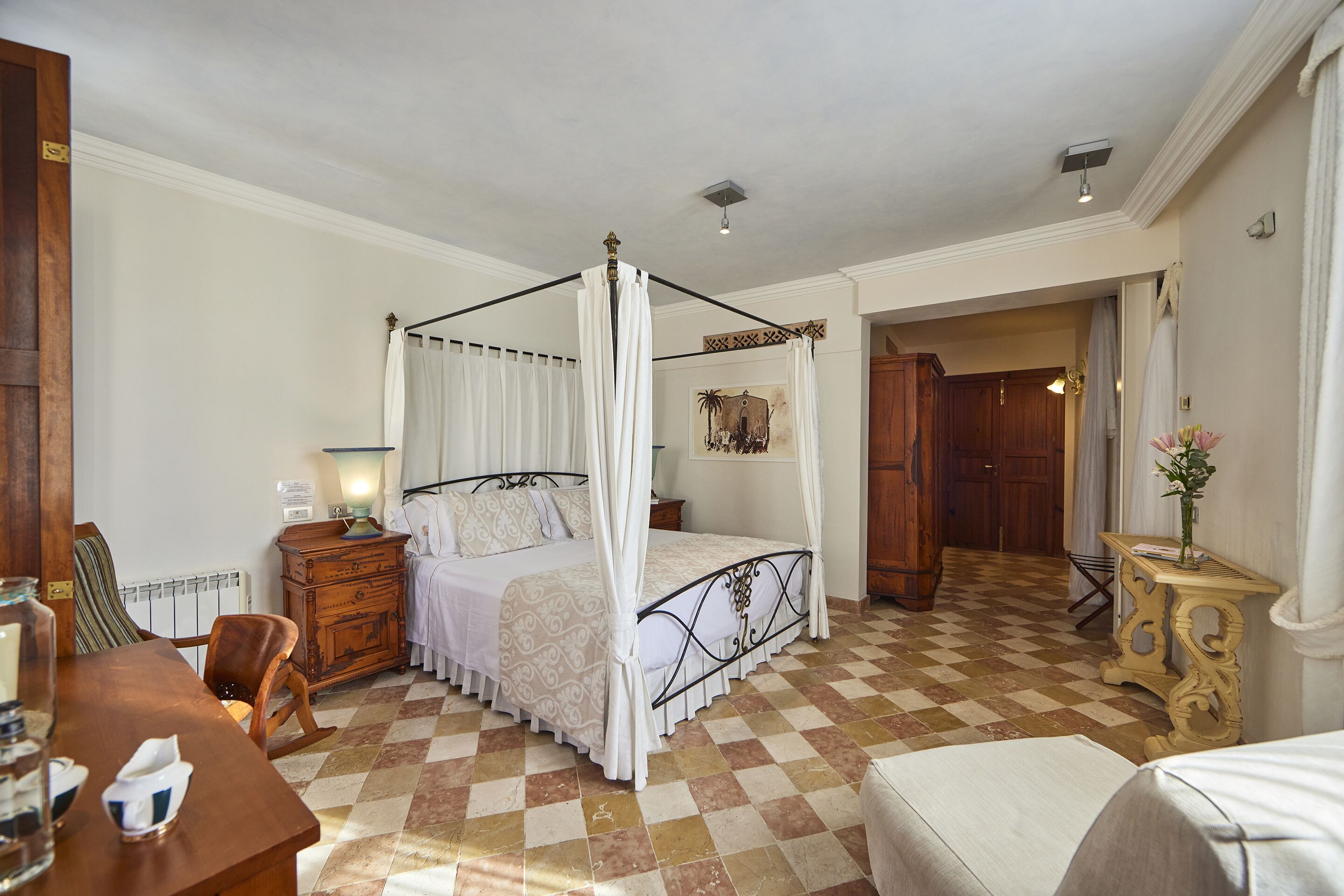 Un dormitorio con cama con dosel, cómoda de madera, una silla y una pequeña mesa con un florero.