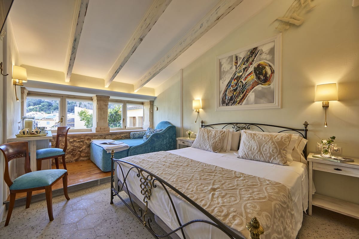 A bedroom with a bed, a desk, chairs, and a window with a view.