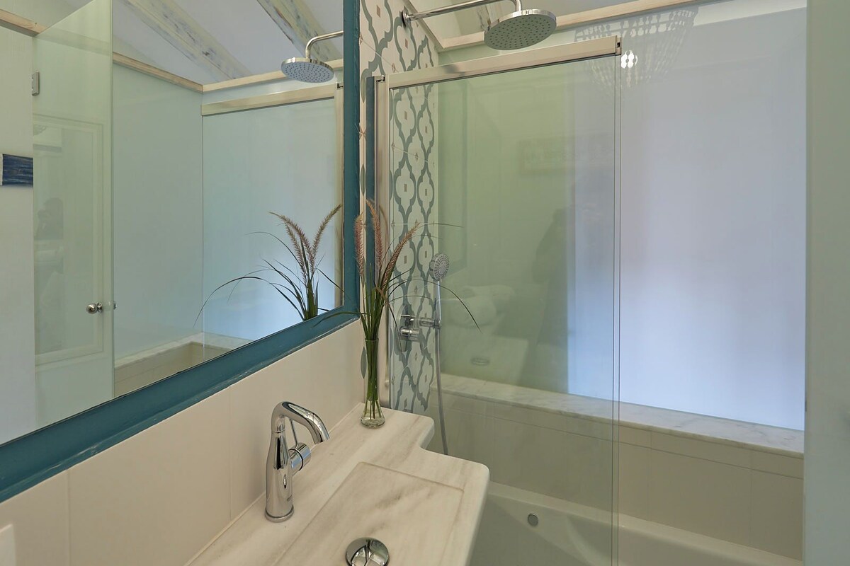 A modern bathroom with a glass shower enclosure, a marble sink, and a large mirror.