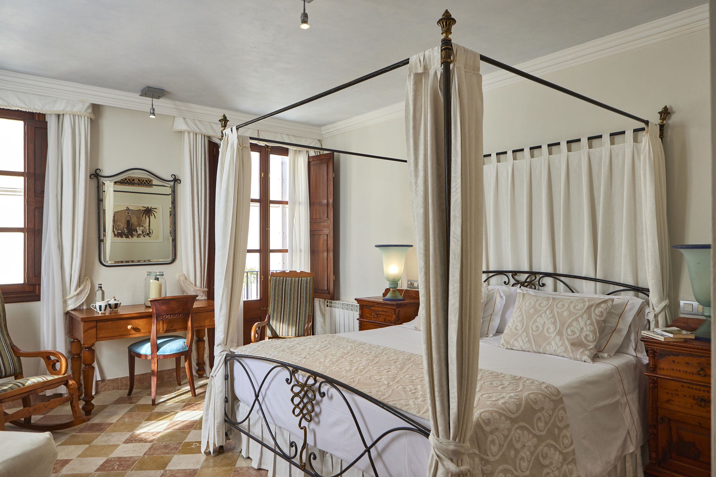 Een bed met hemelbed, houten hoofdeinde, een bureau met stoel, een spiegel en een raam met gordijnen.