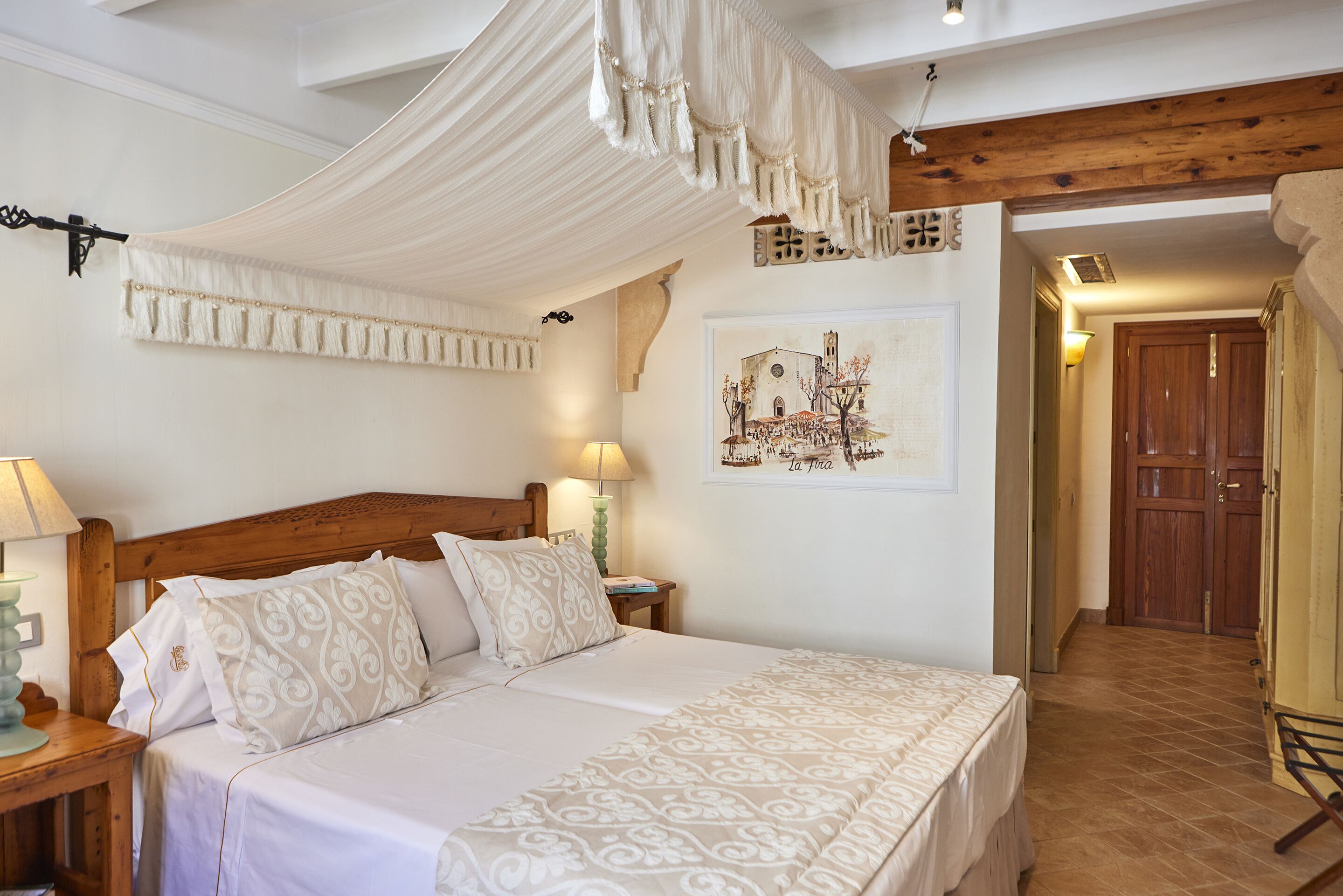 Un dormitorio con cama con dosel, cabecera de madera, mesita de noche con lámpara y una obra de arte en la pared.