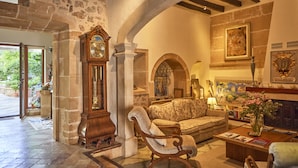A spacious living area with a stone wall, a grand wooden clock, a sofa, a coffee table, and a fireplace. - Son Sant Jordi (Pollenca)