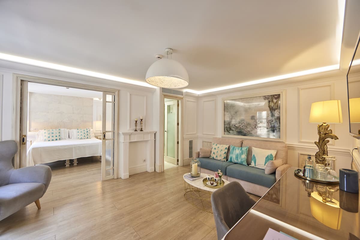A spacious living room with a sofa, armchair, and a coffee table. There is a fireplace and a large window with a view.