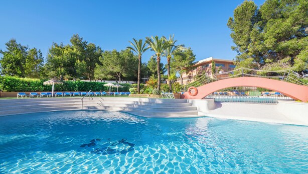 Ein Pool mit klarem, blauem Wasser, umgeben von Liegestühlen und Palmen.