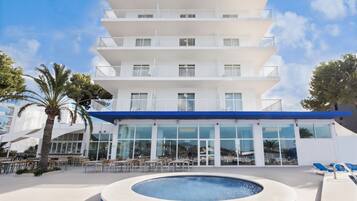 Un hotel de varios pisos con piscina, mobiliario exterior y cielo despejado.