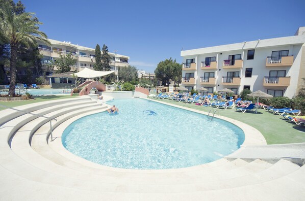 Una piscina con tobogán, rodeada de sillas de descanso y un edificio de varios pisos con balcones.