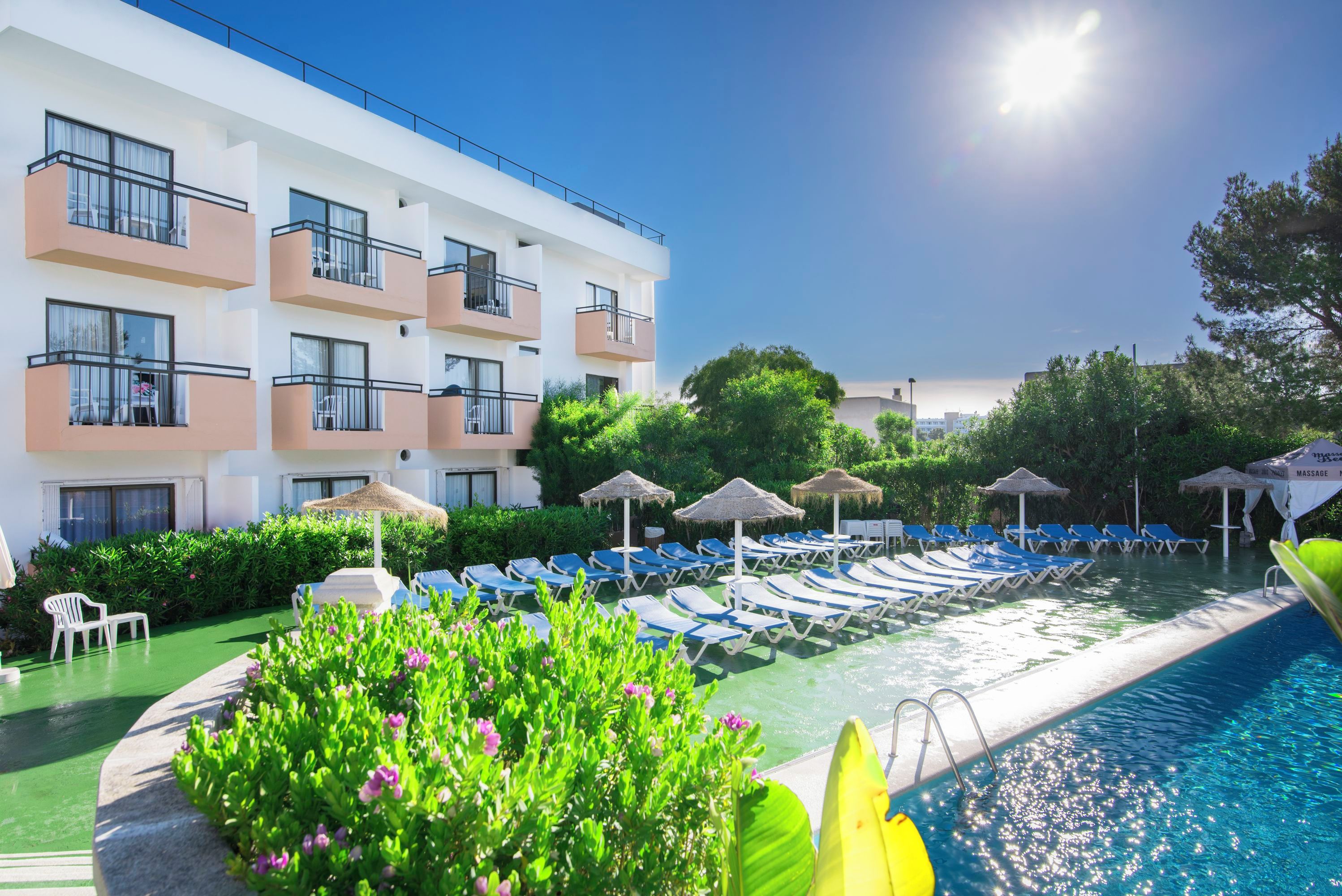 A hotel with a swimming pool, lounge chairs, and a building with balconies.