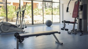 Un gimnasio con equipo de ejercicio, una banca y ventanas amplias con vistas a zonas verdes.