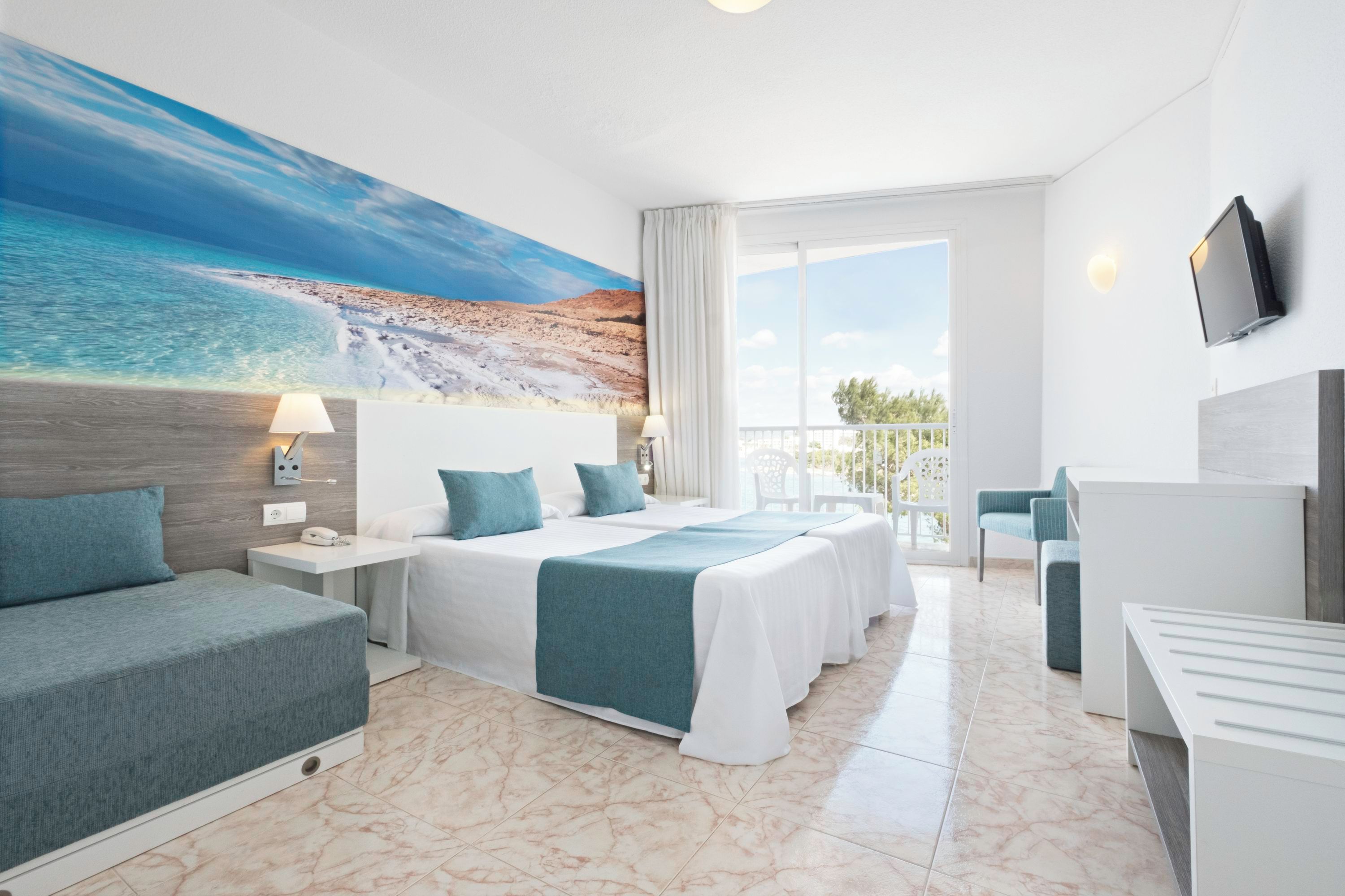 Ein Hotelzimmer mit einem großen Bett, einer Sitzecke, einem Schreibtisch und einem Balkon mit Meerblick.