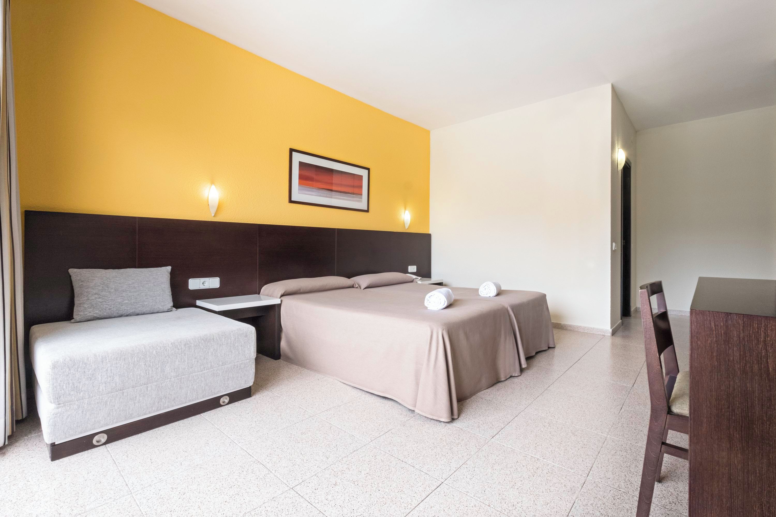 Una habitación de hotel con cama, mesitas de noche, un escritorio y una silla.