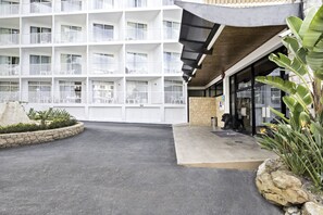 Un hotel de varios pisos con un patio central, que presenta una jardinera de piedra con plantas tropicales y una estatua.