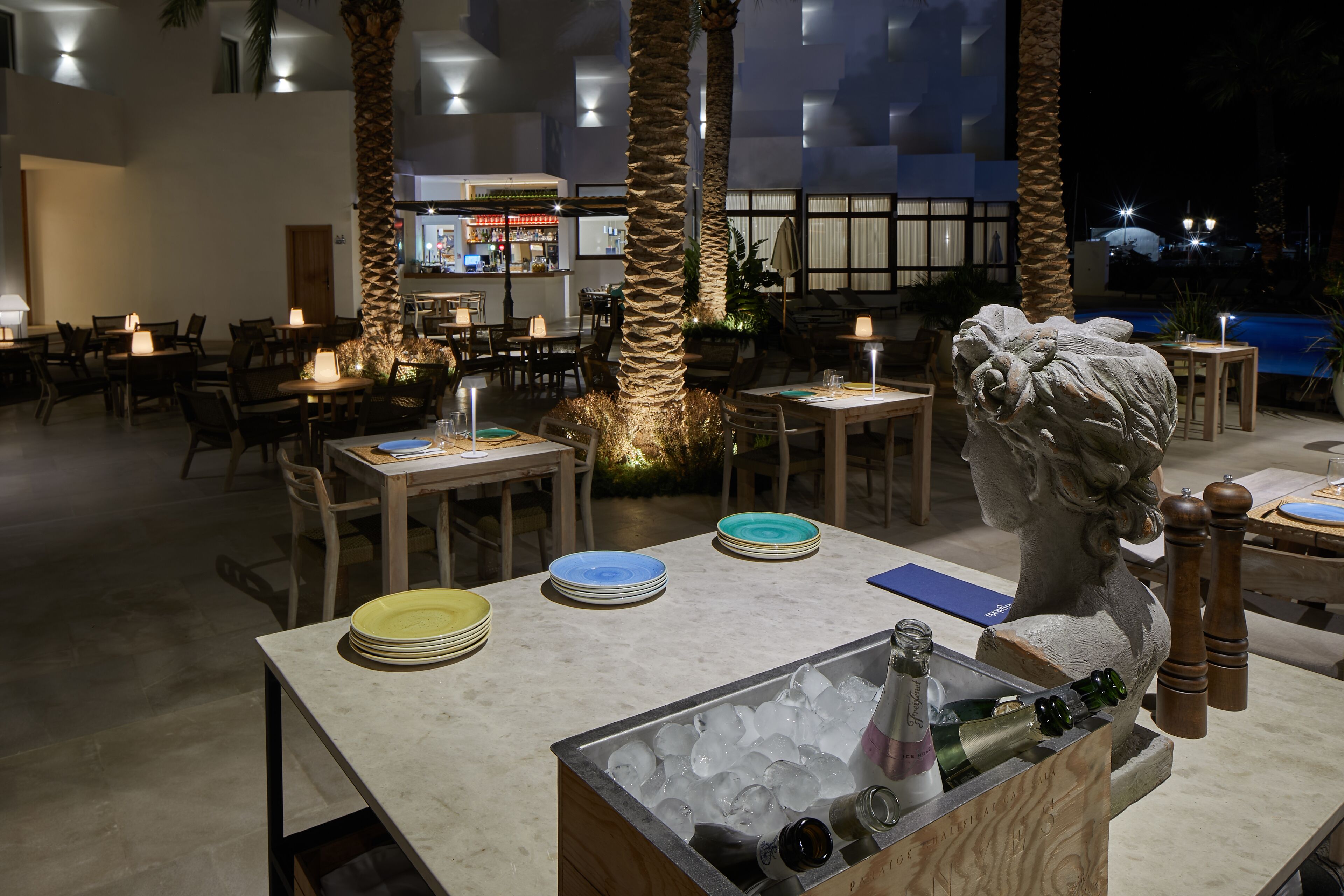 A restaurant with tables set for dining, a bar in the background, and a statue centerpiece.