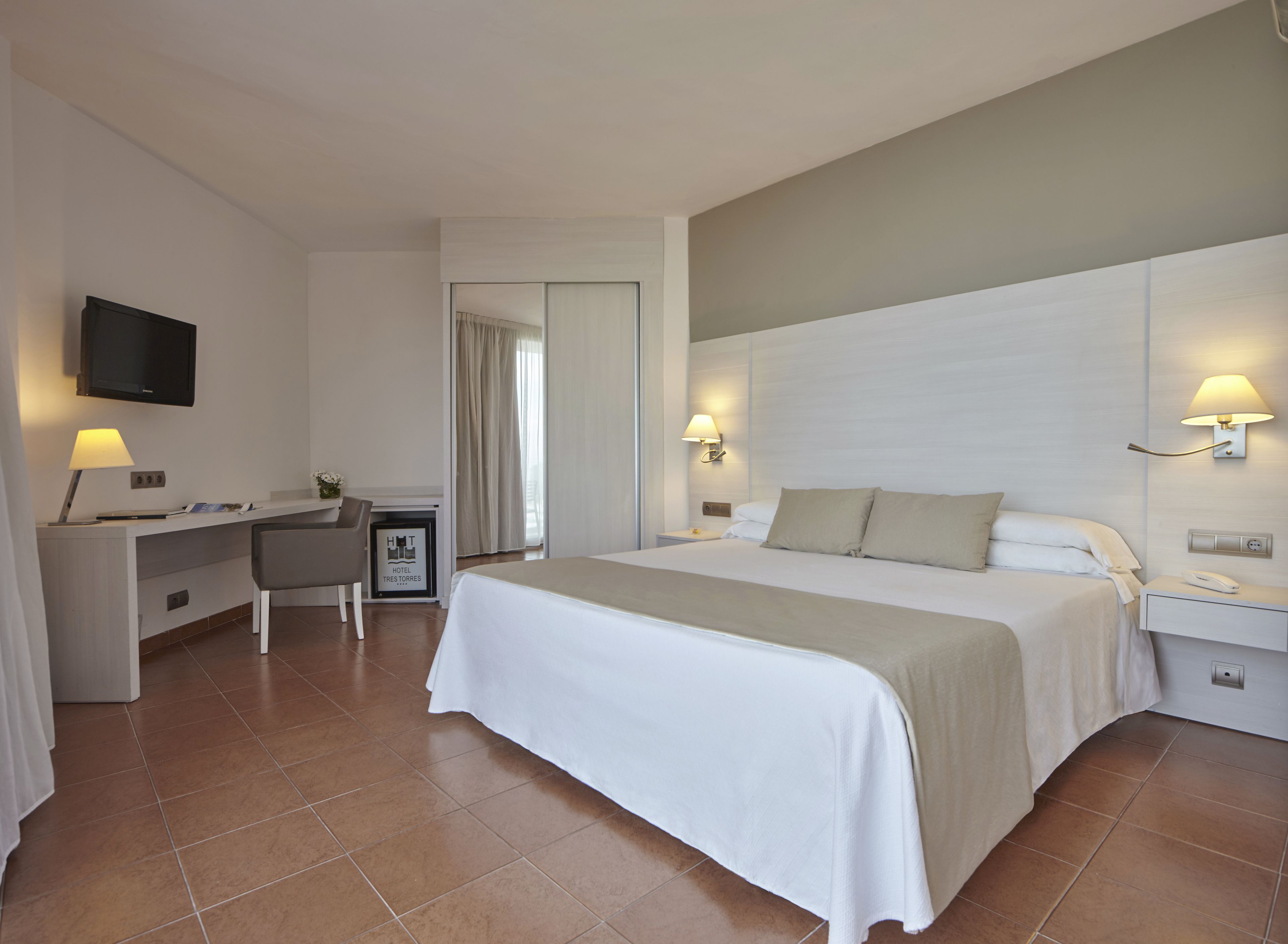 A hotel room with a bed, desk, chair, TV, and two bedside lamps.