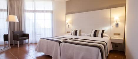 A hotel room with a large bed, two bedside lamps, a chair, and a window with curtains.