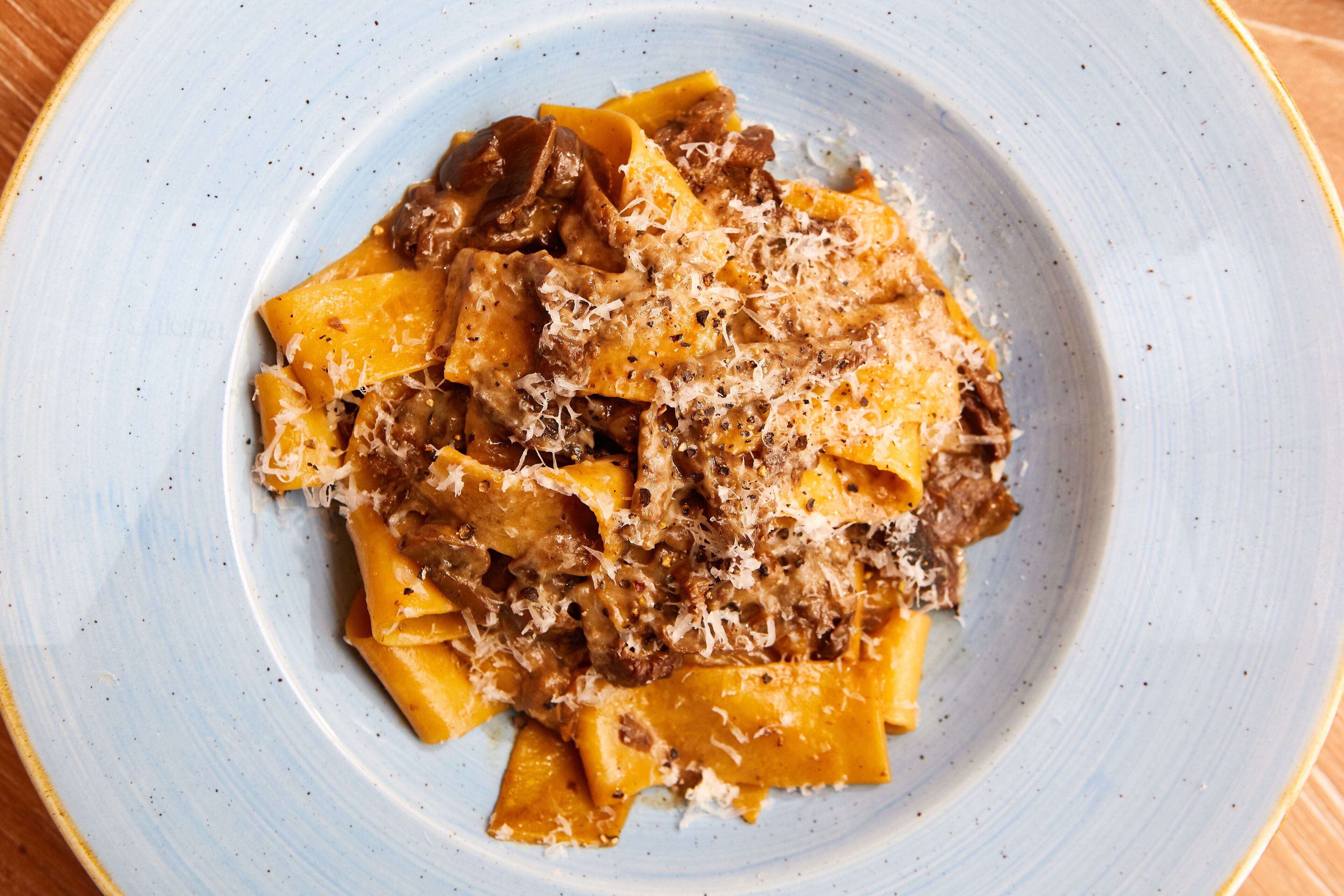 Un plato de pasta con salsa cremosa y queso rallado sobre un plato azul.