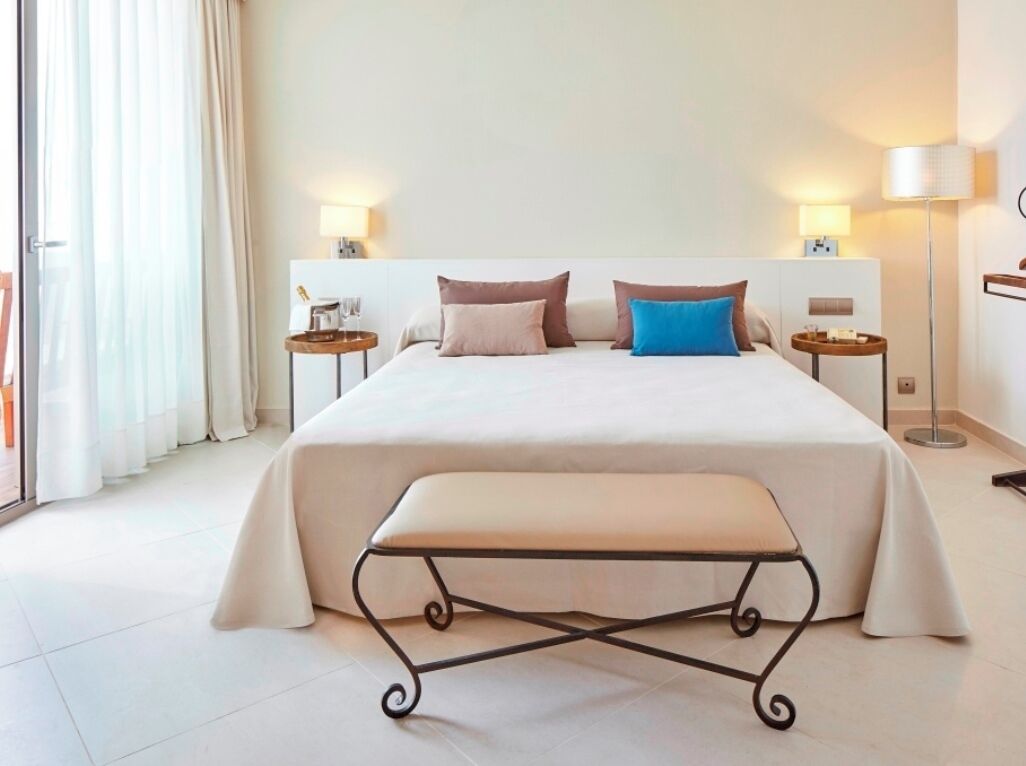 Een hotelkamer met een groot bed, twee nachtkastjes, een bankje en uitzicht op het omliggende landschap.